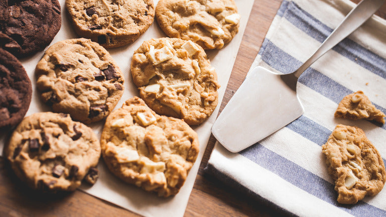 Assorted cookies on a baking sheet with a spatula and striped towel.